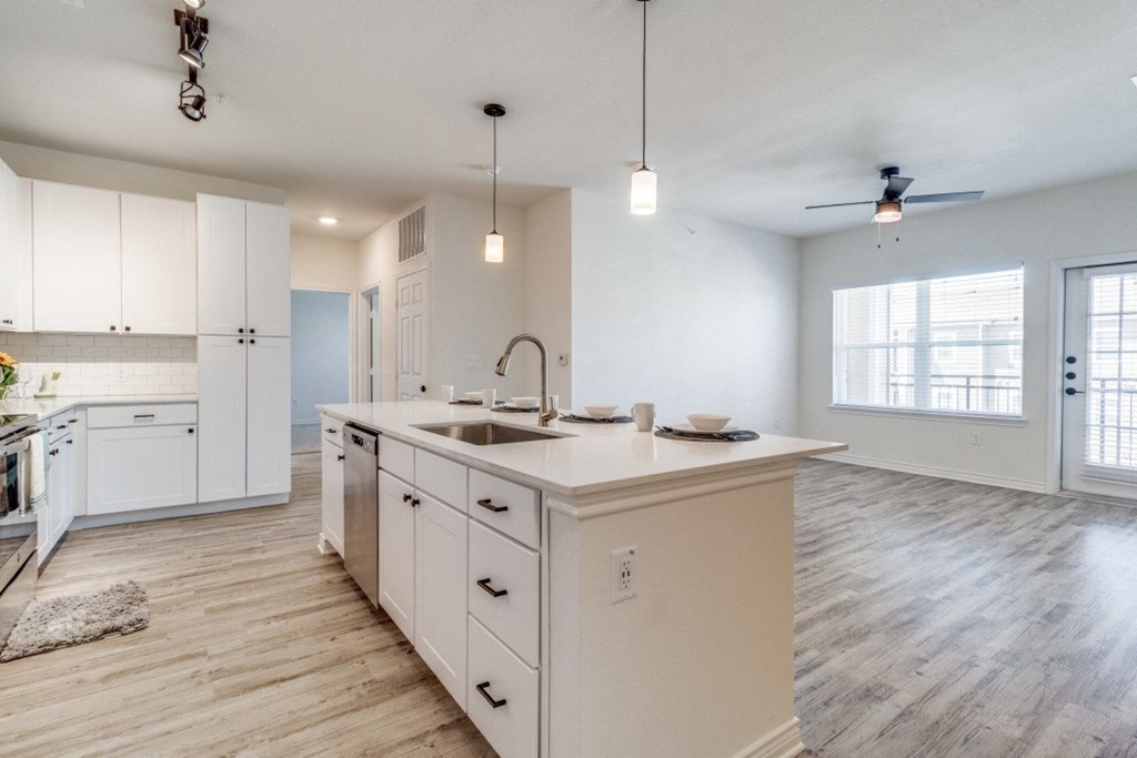 an open kitchen and living room with white cabinets and a large counter top