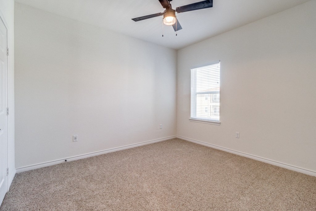 an empty bedroom with a ceiling fan and a window