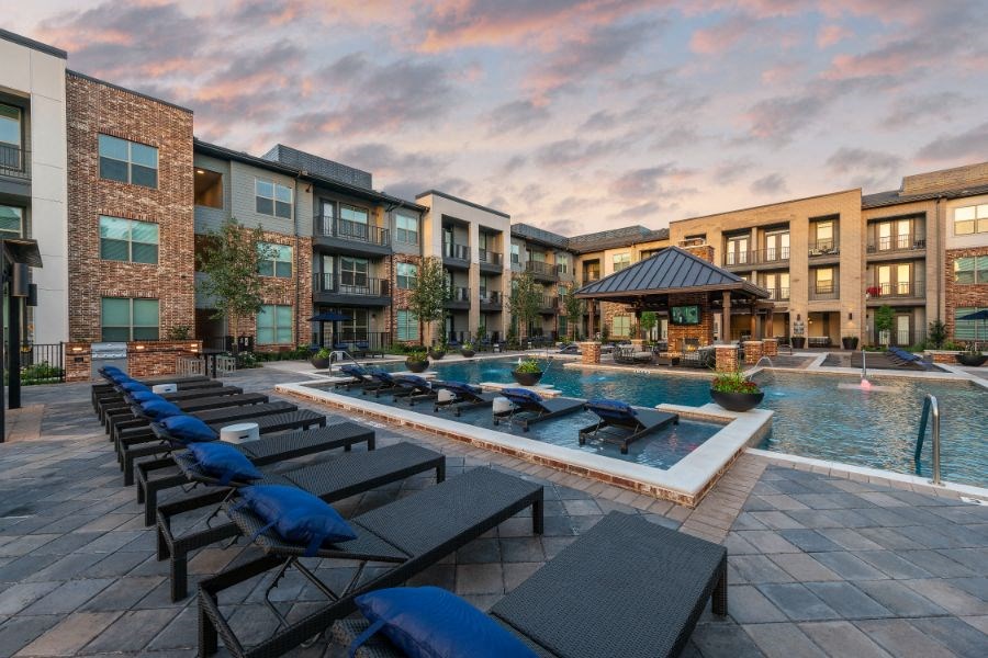 a pool with lounge chairs in front of an apartment building