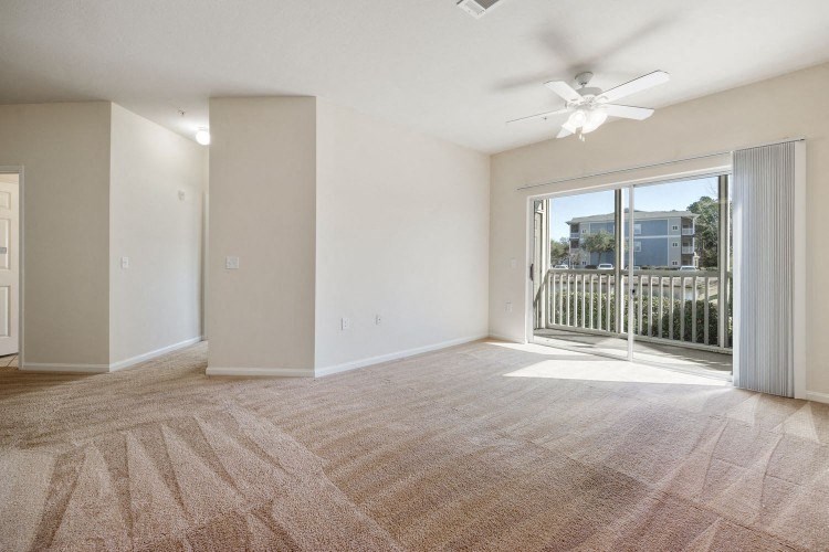an empty living room with a balcony and a ceiling fan