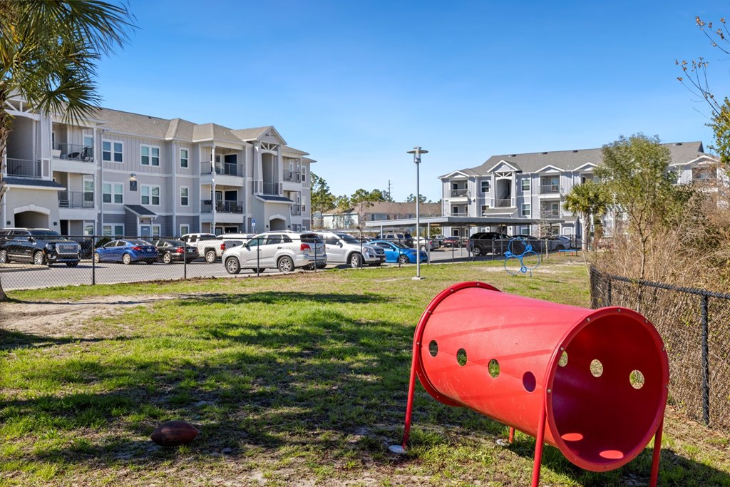 A red tunnel-like structure with holes in it is in the foreground of a grassy area.