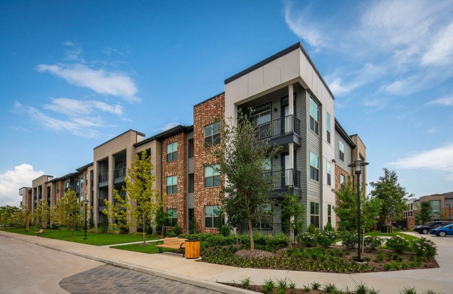 an apartment building with a sidewalk and trees in front of it