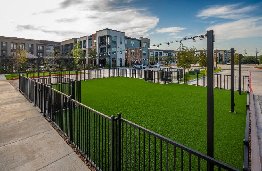 a green lawn in front of a building with a fence