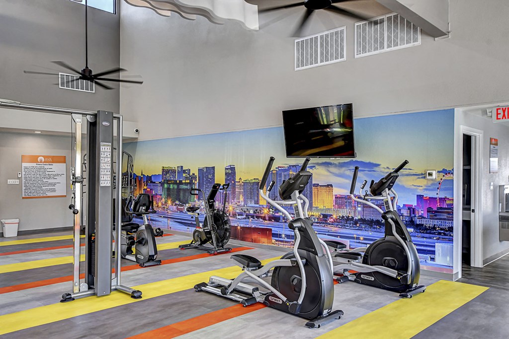 a gym with cardio equipment and a mural of a city on the wall