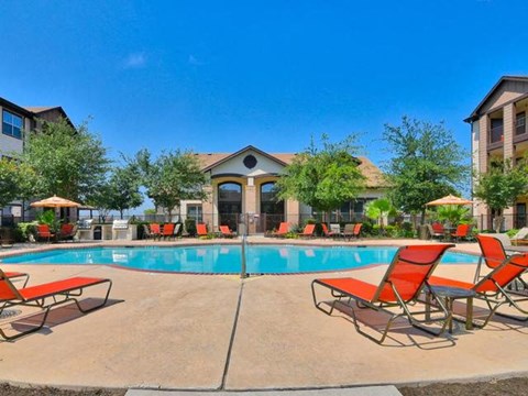 A swimming pool surrounded by red chairs and umbrellas.