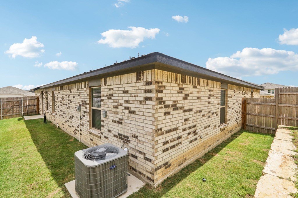A house with a brown brick wall and a black roof with a fence and a green lawn.