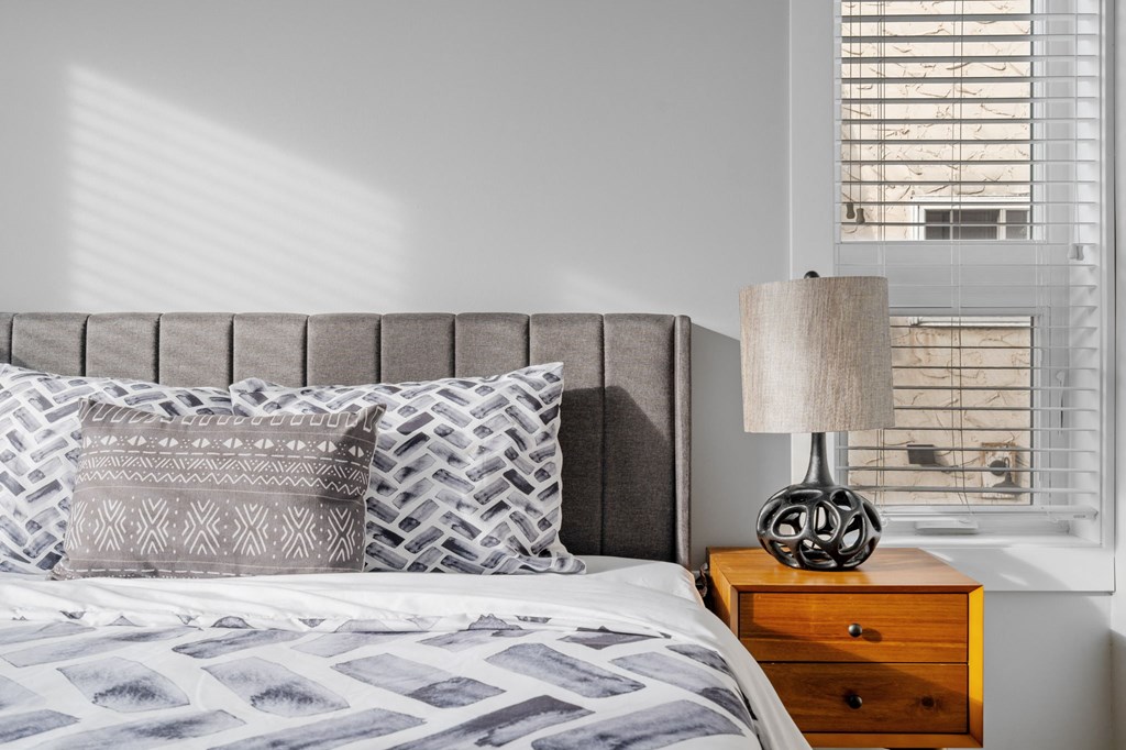 a bedroom with a bed and a dresser with a lamp and a window