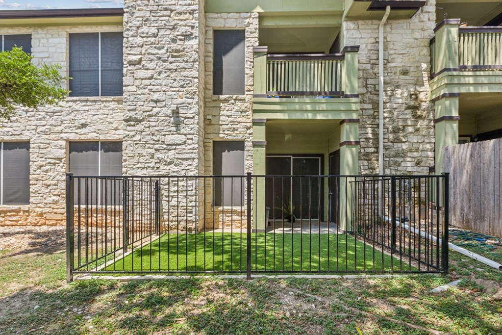 A black iron fence surrounds a green lawn in front of a stone building.