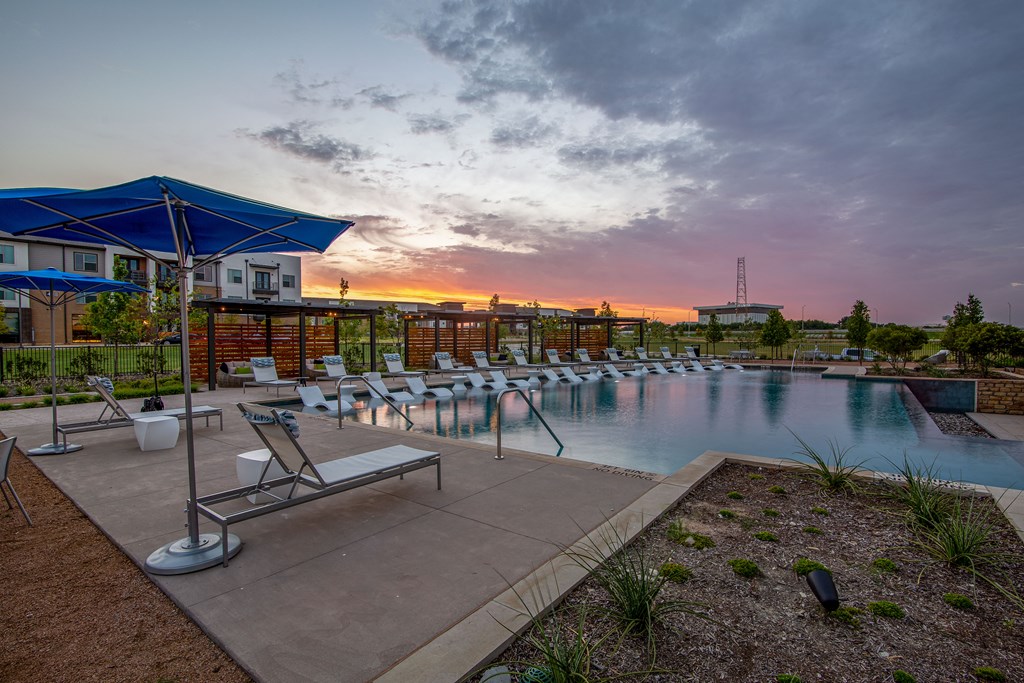 a swimming pool with chairs and umbrellas at sunset