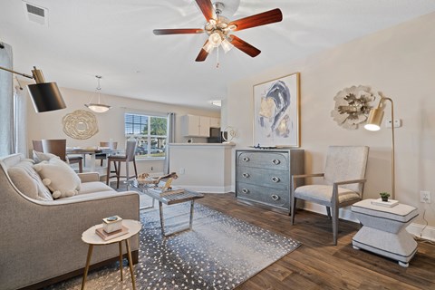 A living room with a fan, a couch, a chair, a coffee table, and a painting on the wall.