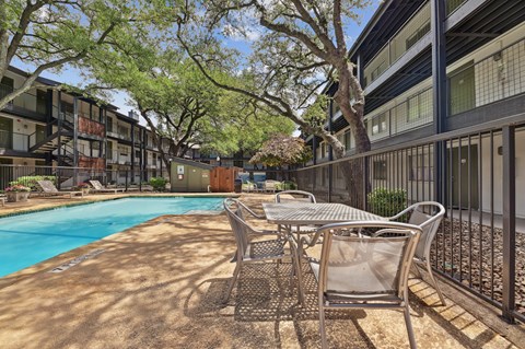 A pool surrounded by chairs and trees in a sunny courtyard.
