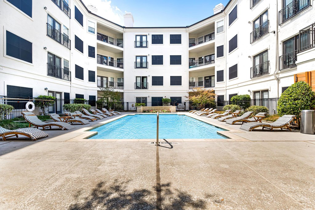 a swimming pool with chaise lounge chairs and an apartment building in the background