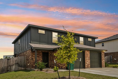 A modern house with a grey roof and a tree in front.