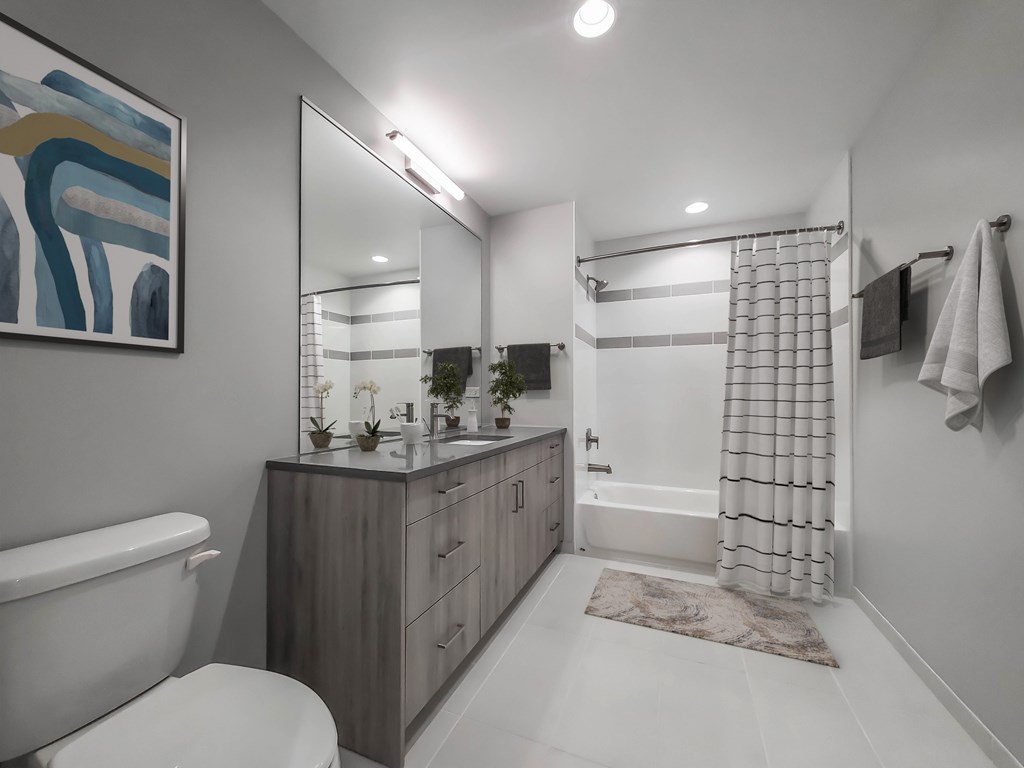 A modern bathroom with a white toilet, a wooden vanity, and a shower area.