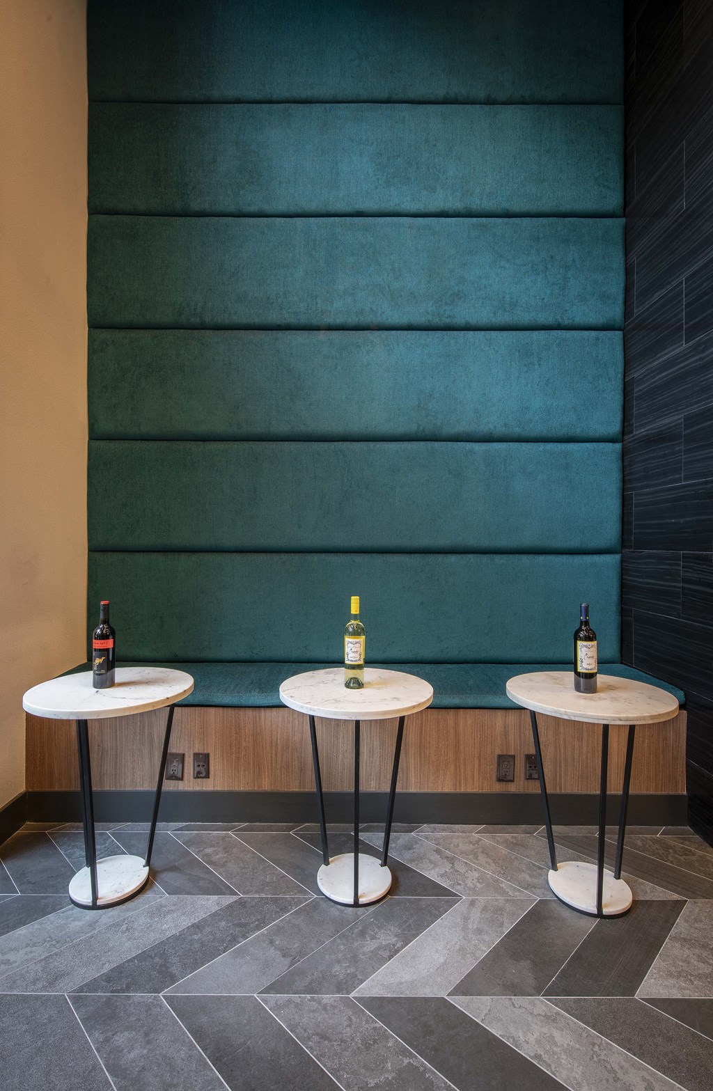 a trio of tables in front of a teal wall with two bottles of wine on top