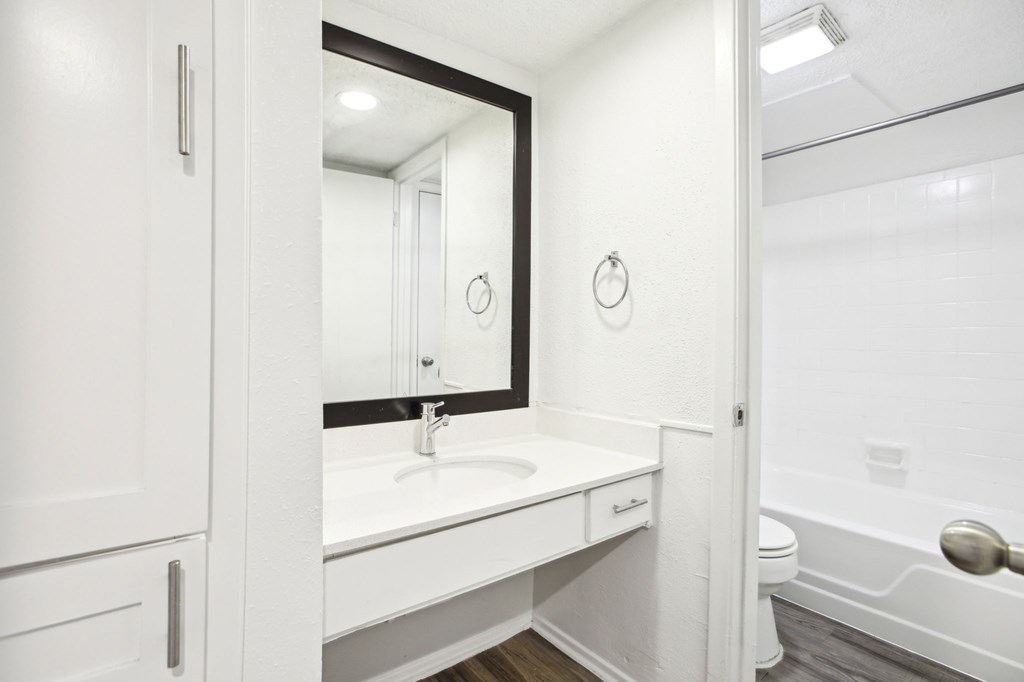 A white bathroom with a sink, mirror, and toilet.