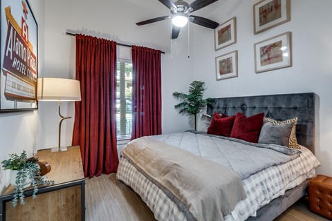 A bedroom with a bed, a ceiling fan, and a window with red curtains.