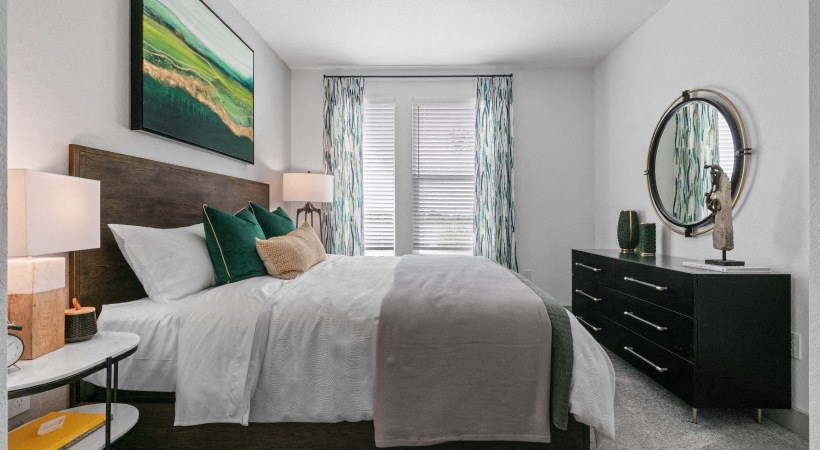 A bedroom with a large bed, a side table with a lamp, and a painting on the wall.