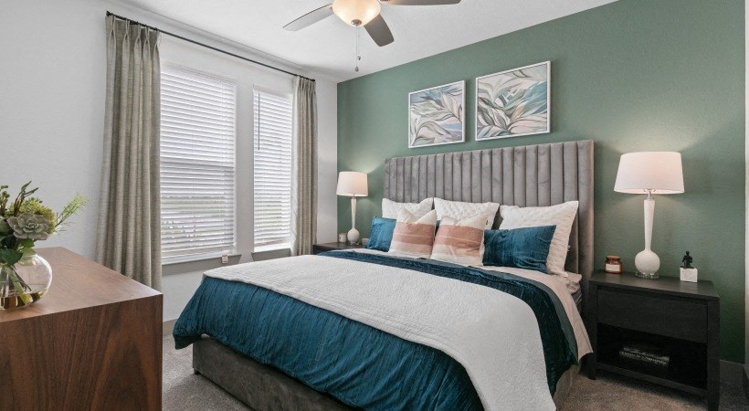 A bedroom with a bed, nightstand, and a plant.