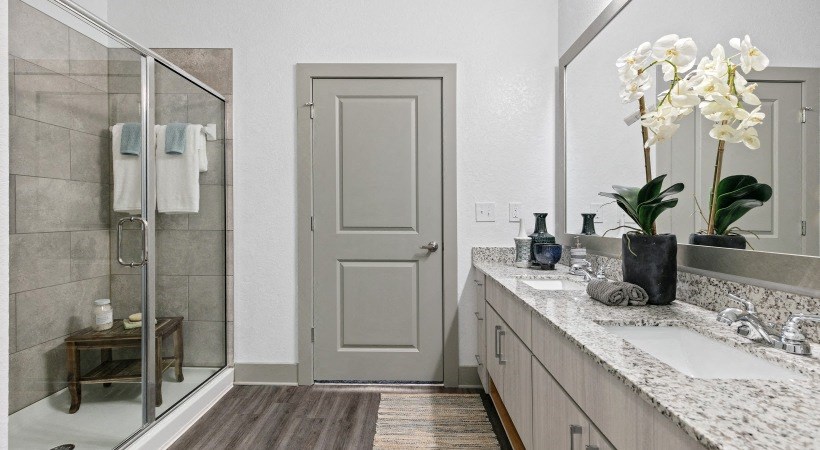 A bathroom with a grey door, a glass shower stall, and a marble countertop.