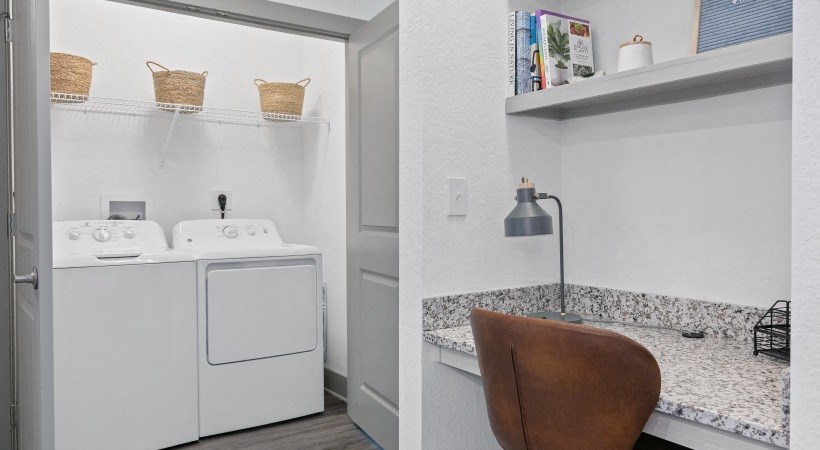 A laundry room with a washer and dryer and a kitchen area with a counter and a chair.