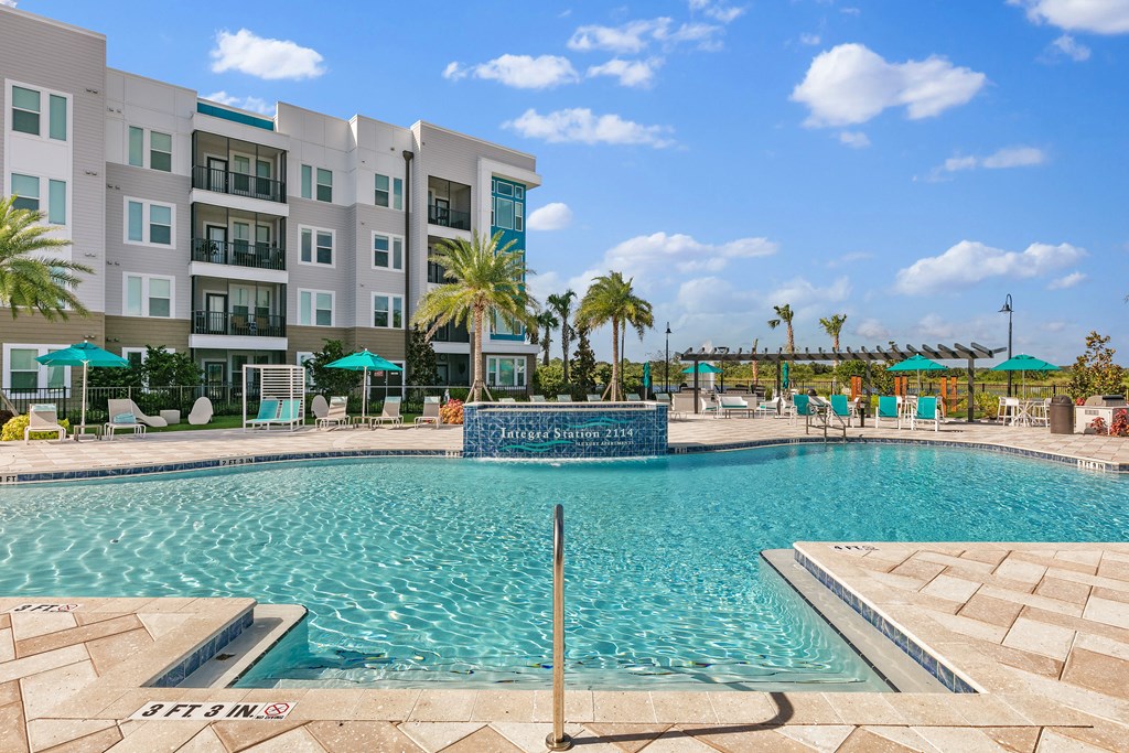 A swimming pool in front of a multi-story building with palm trees.