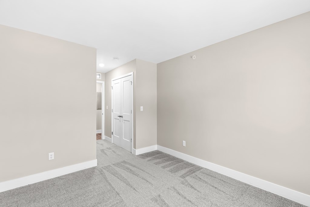 an empty living room with gray carpet and a white door
