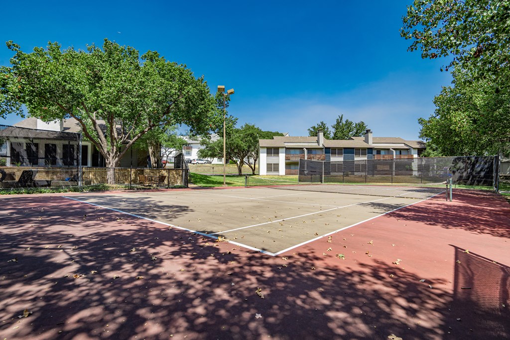 a tennis court with trees and a building in the background