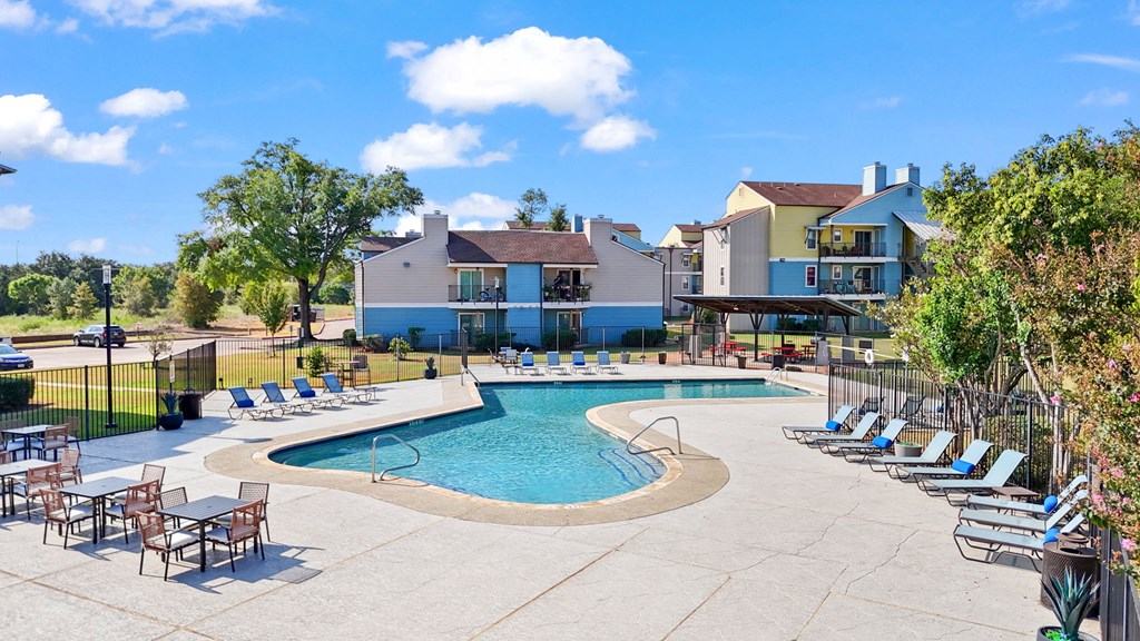 A large outdoor swimming pool surrounded by lounge chairs and trees.