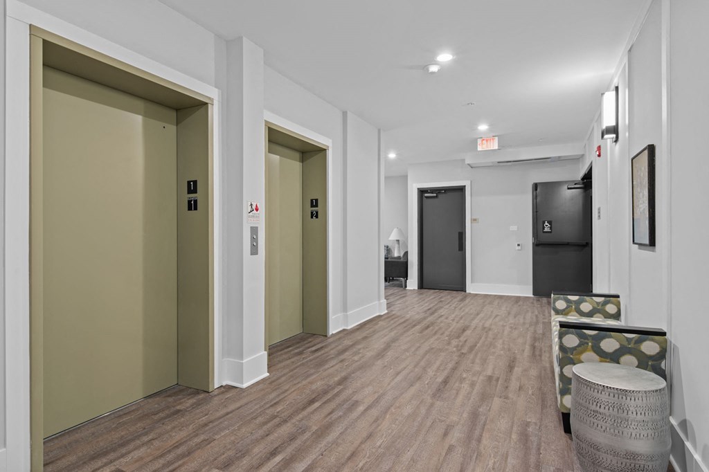 a long hallway with white walls and wood floors and a lobby with chairs and doors