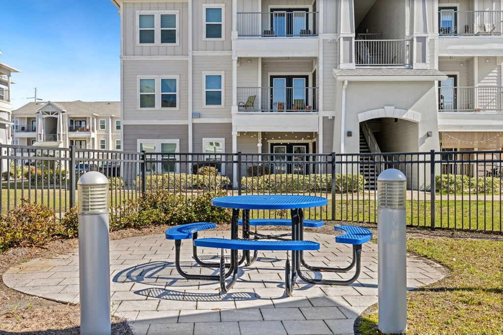 A blue picnic table sits in front of a black fence and apartment building.