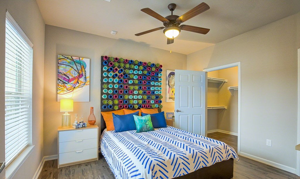 A bedroom with a bed, a ceiling fan, and a wall hanging.