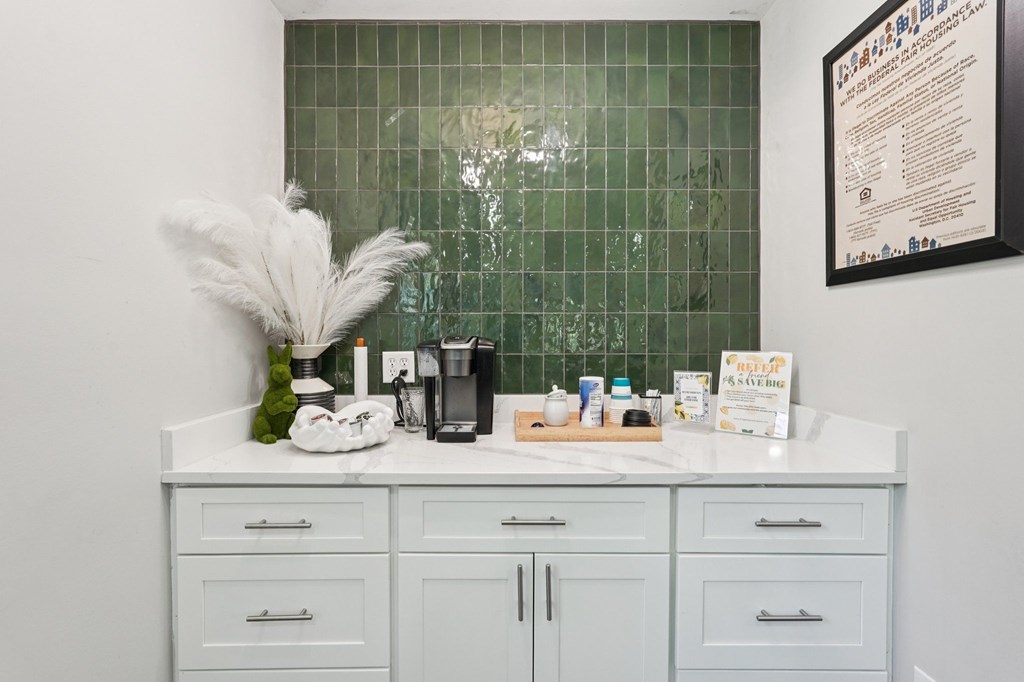 A bathroom with a white counter and a green tiled wall.