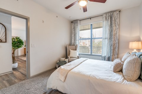A bedroom with a large bed, a ceiling fan, and a window with blinds.