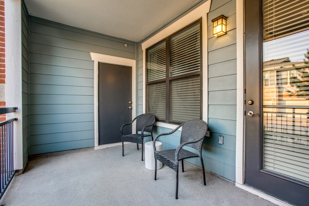 the front porch of a house with two chairs and a door