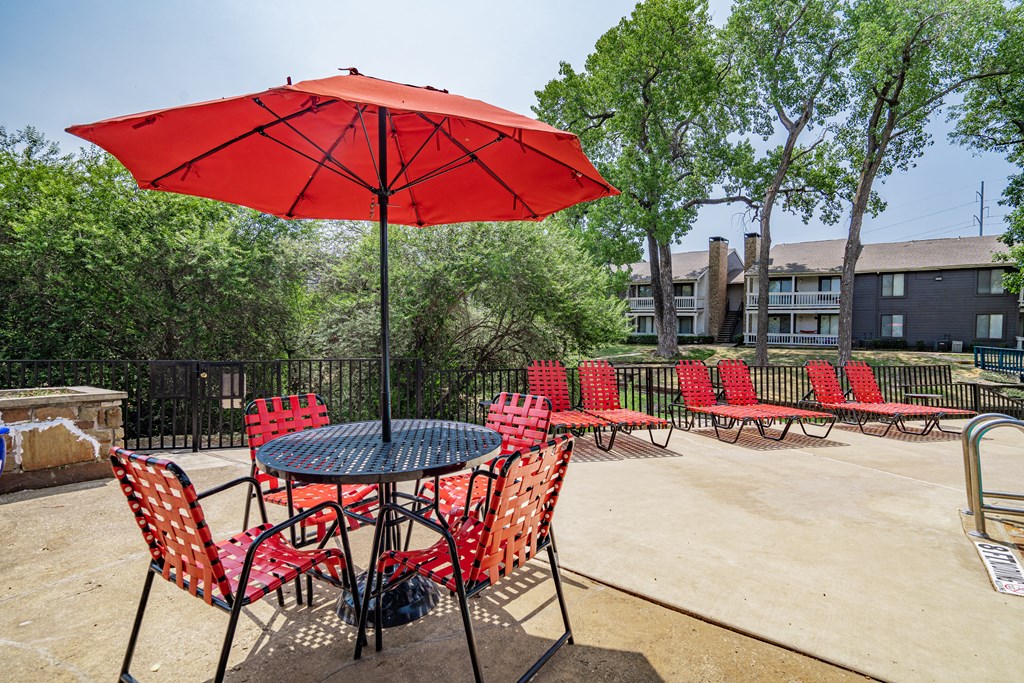 a patio with tables and chairs and a red umbrella