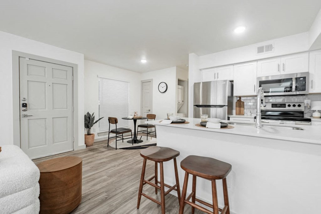 A kitchen with white cabinets and a bar area with stools.