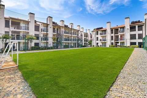 a grassy area with a swing set in front of an apartment complex