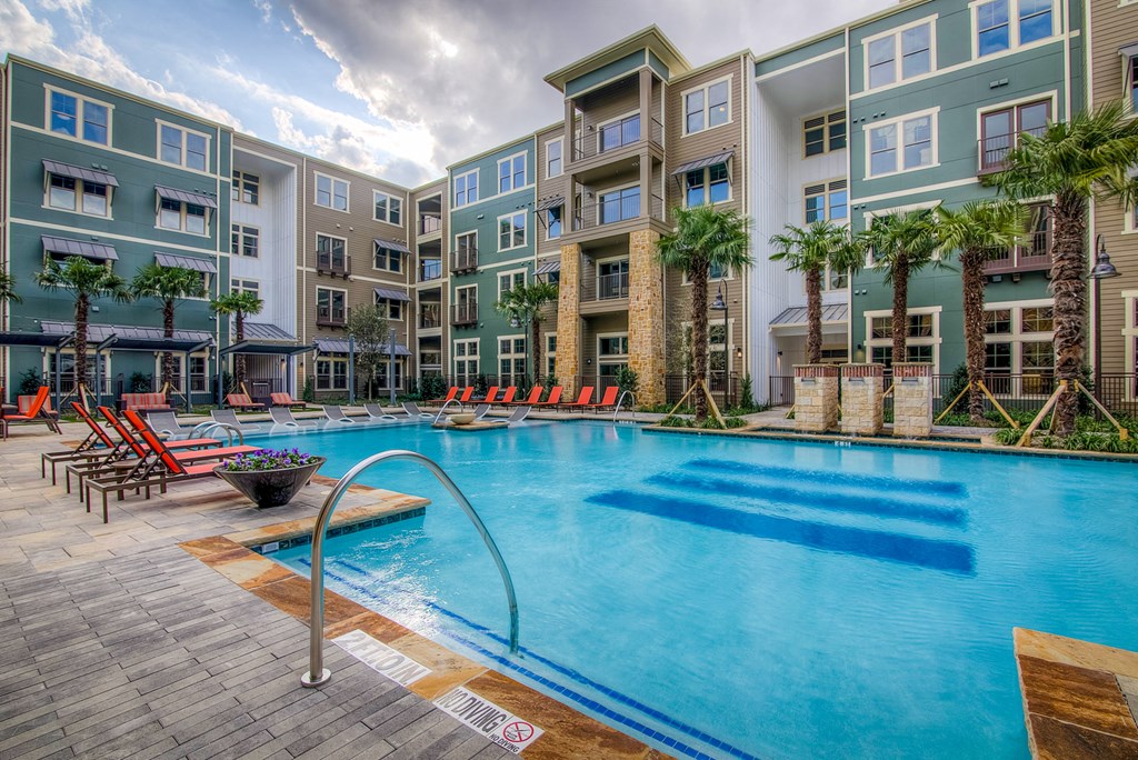 an outdoor pool with lounge chairs and a firepit in front of an apartment building