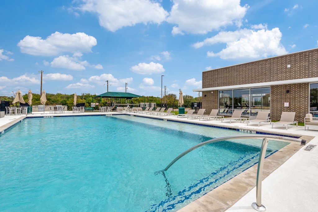a swimming pool with lounge chairs and umbrellas next to a brick building