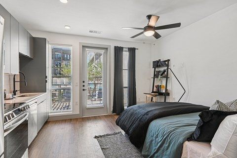 A modern bedroom with a large bed and a kitchen area in the background.