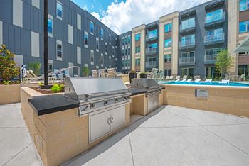 two gas grills on a patio next to a pool in front of an apartment