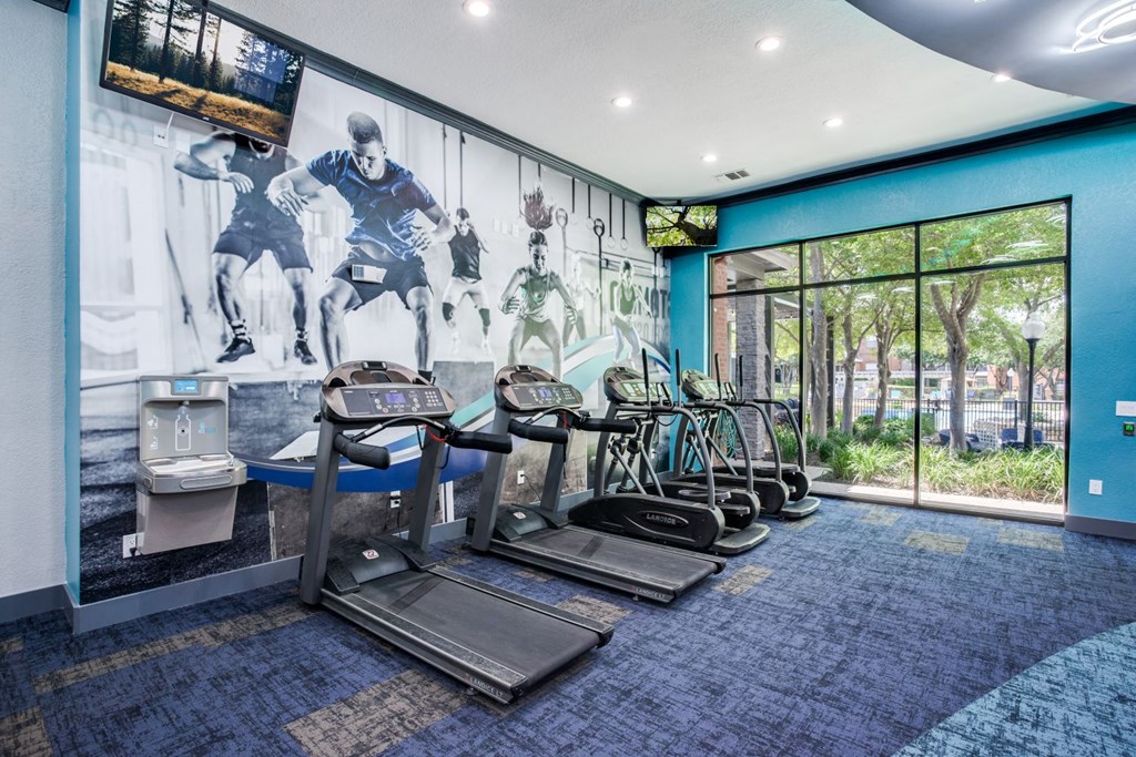 a gym with cardio machines and a mural of soccer players on the wall