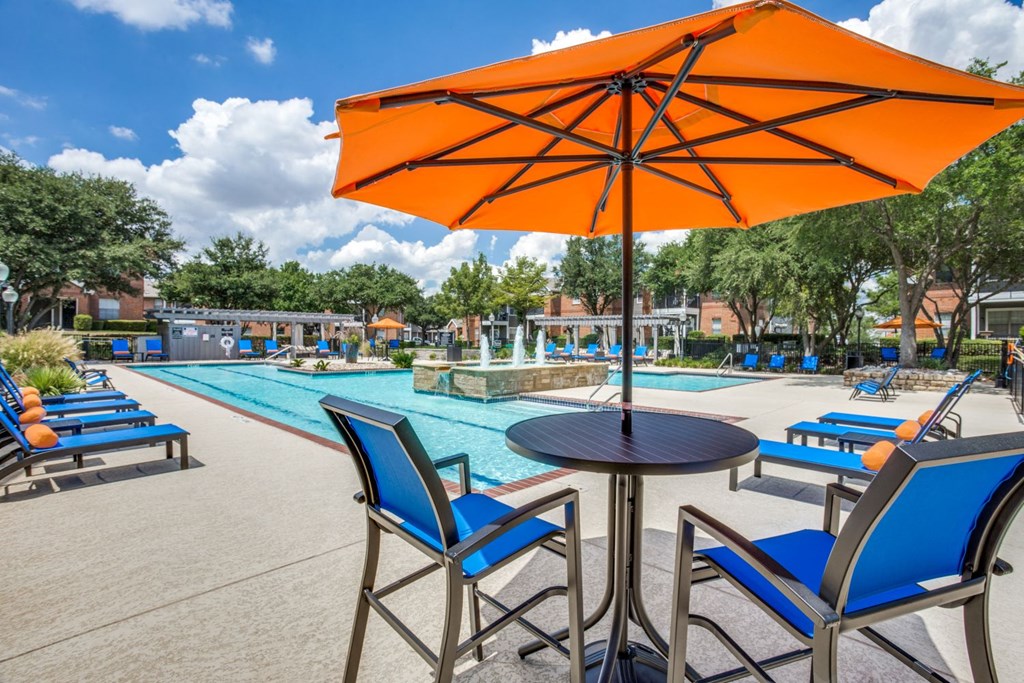 a table with an orange umbrella and chairs near a swimming pool