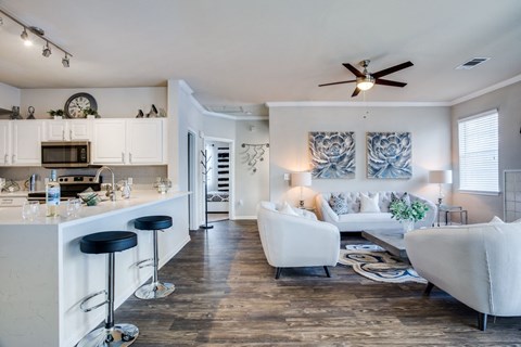 a living room and kitchen with white furniture and a ceiling fan