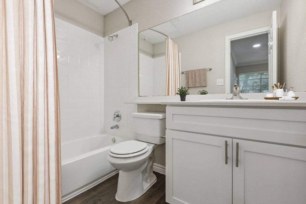 A white toilet sits in a bathroom with a white tub and a white sink.