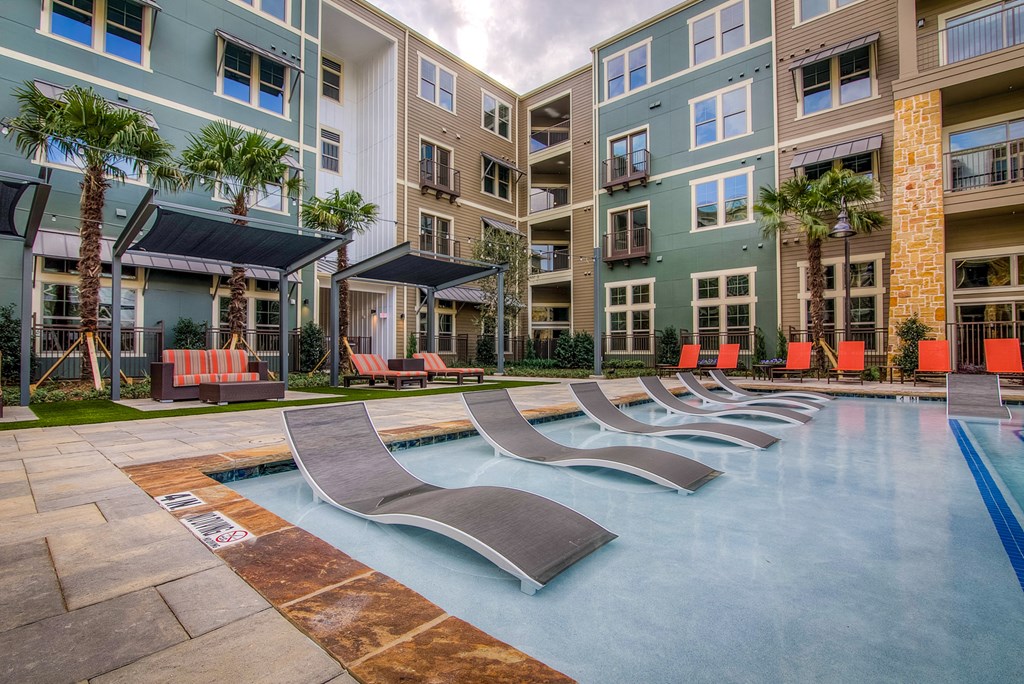 an outdoor pool with chaise lounge chairs and an apartment building in the background