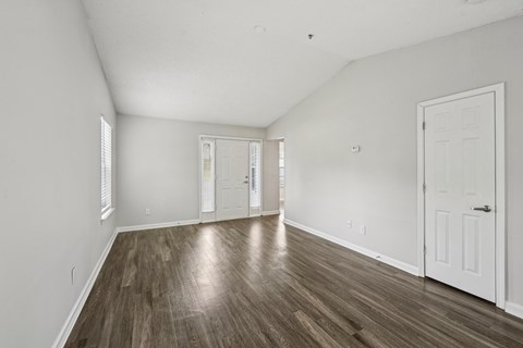 A room with white walls and wood flooring with a door on the right.
