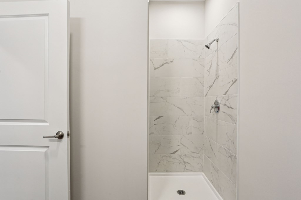 A white door is open to a bathroom with a marble shower.