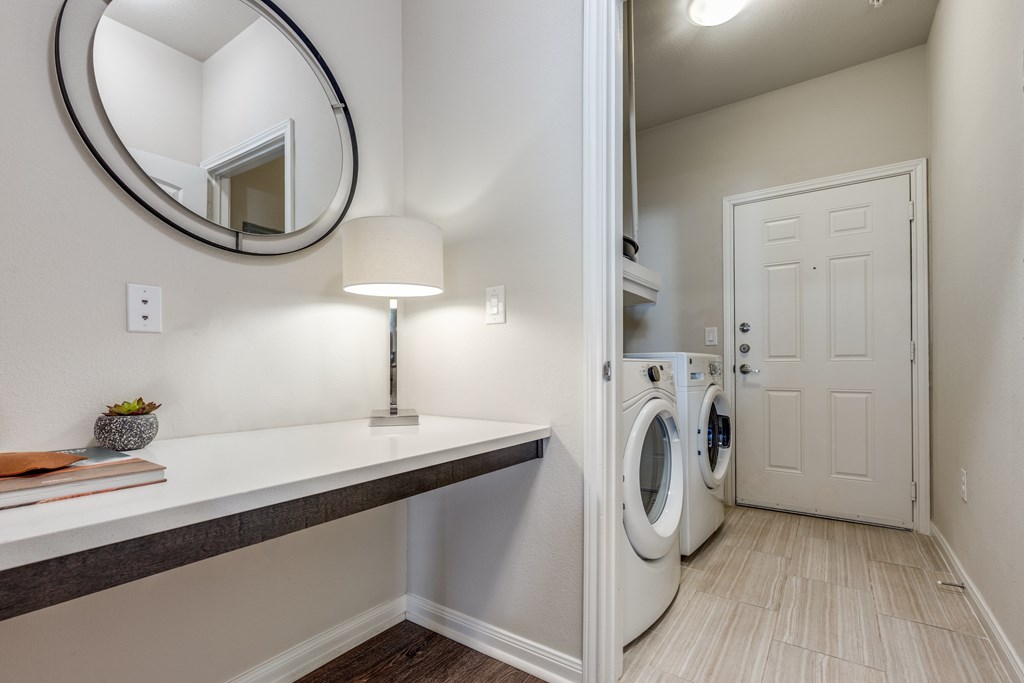 A laundry room with a washer and dryer, a counter, and a round mirror.